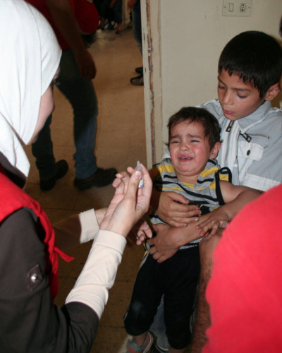 A volunteer of the Syrian Arab Red Crescent administers oral polio vaccine to a crying child as part of a campaign to extinguish an outbreak of the disease in 2014.